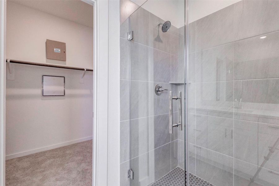 Primary shower detail featuring a glass enclosure, gray tile surround, built-in corner shelf, and modern chrome fixtures. The nearby walk-in closet adds everyday convenience, while the neutral tile palette and clean lines give the bath a fresh, spa-like feel designed for comfort, function, and easy maintenance. Primary shower detail featuring a glass enclosure, gray tile surround, built-in corner shelf, and modern chrome fixtures. The nearby walk-in closet adds everyday convenience, while the neutral tile palette and clean lines give the bath a fresh, spa-like feel designed for comfort, function, and easy maintenance.