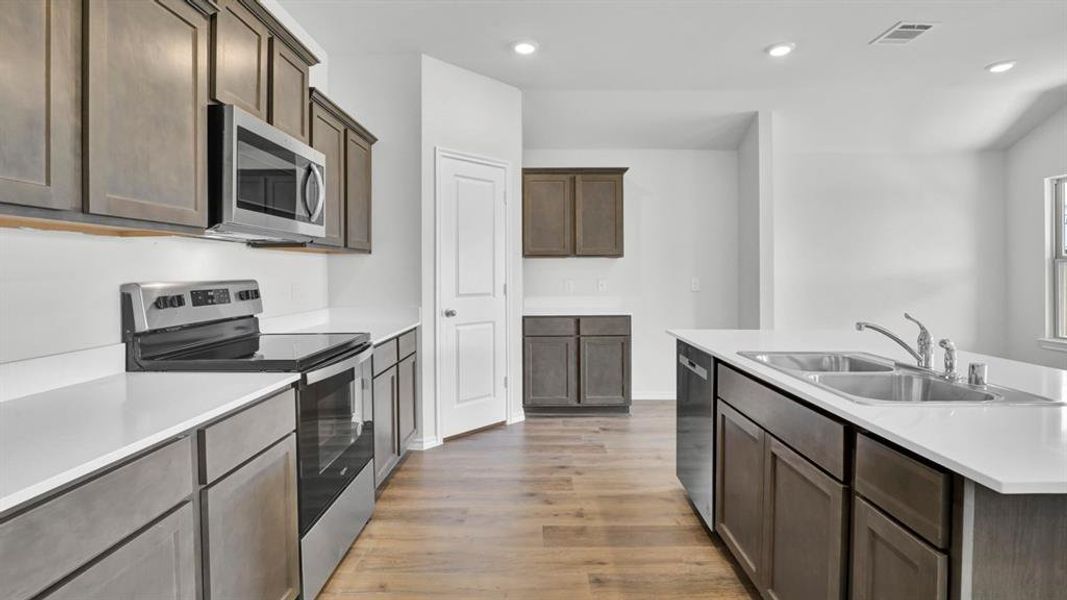 Kitchen featuring stainless steel appliances, light wood-type flooring, a kitchen island with sink, recessed lighting, and dark wood finish cabinetry