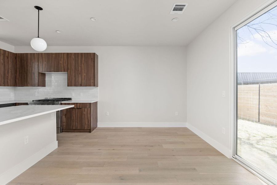 Kitchen with light wood-type flooring, visible vents, tasteful backsplash, light countertops, and gas range