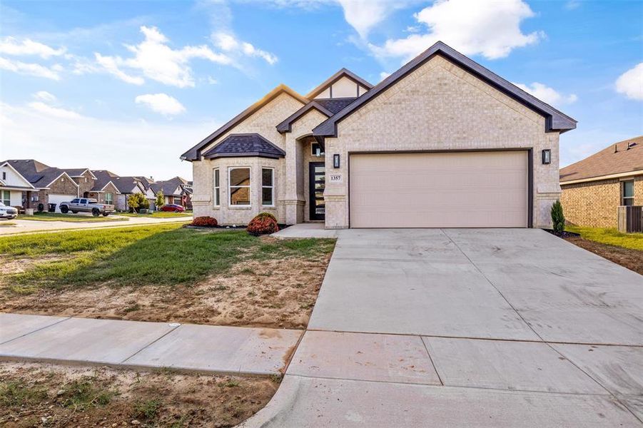 French country inspired facade featuring brick siding, driveway, a garage, a front yard, and a residential view