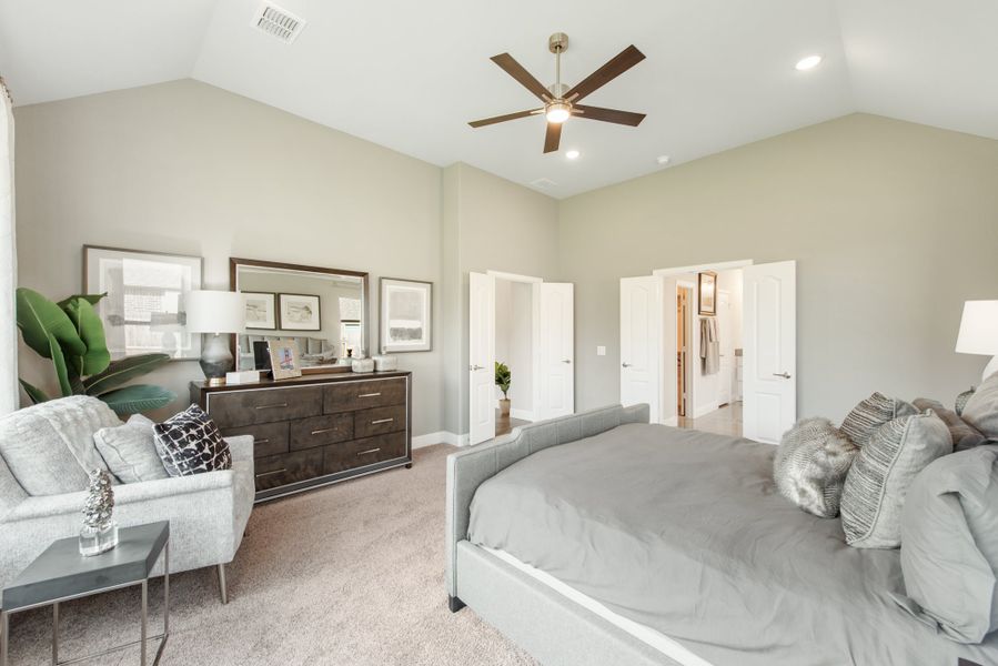 Master bedroom with vaulted ceiling, ceiling fan, dark wood dresser, and open doors to bathroom and closet