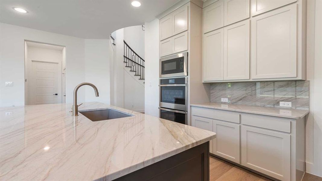 Kitchen featuring built in microwave, stainless steel double oven, backsplash, recessed lighting, and light stone countertops
