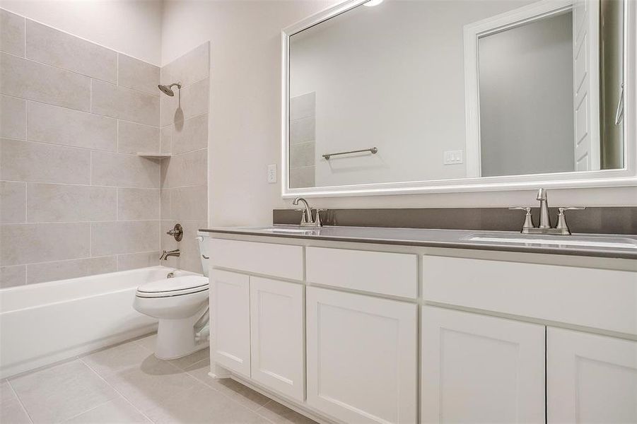 Full bathroom featuring dual vanity, tiled shower / bath combo, toilet, and tile patterned floors