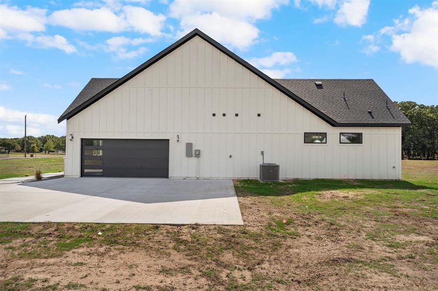 View of home's exterior featuring concrete driveway, a shingled roof, a yard, and board and batten siding