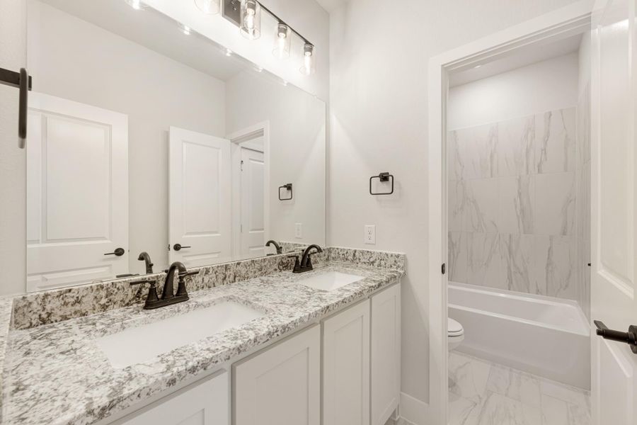 Bathroom with double granite vanity, large mirror, and marble-tiled tub surround