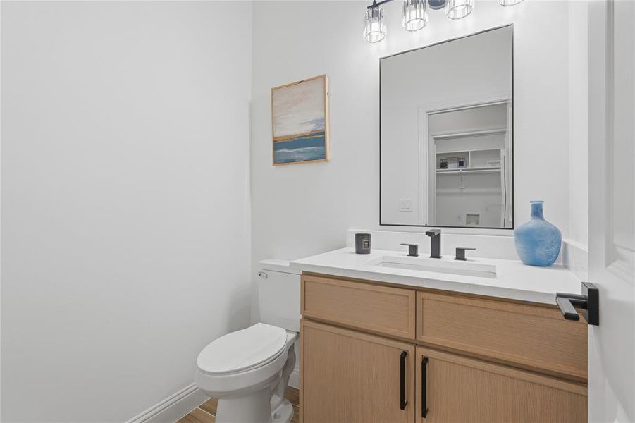 Powder room featuring a wood-finish vanity with black hardware, white countertop, integrated rectangular sink, and matte black faucet Powder room featuring a wood-finish vanity with black hardware, white countertop, integrated rectangular sink, and matte black faucet