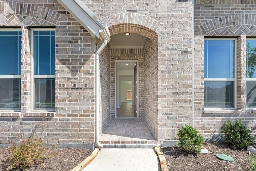 Brick home entrance with arched doorway, covered entry, and concrete walkway leading to front door