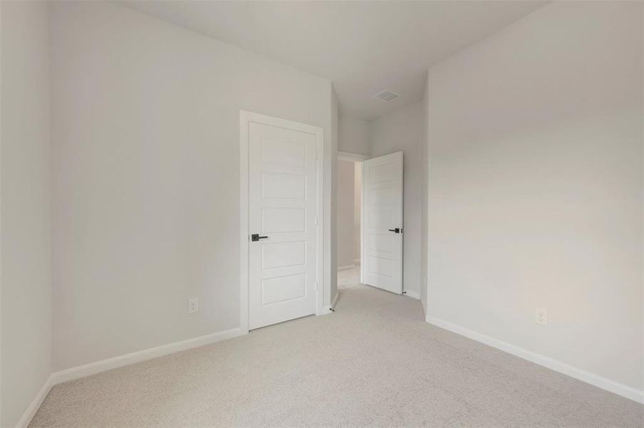 Carpeted interior space featuring light-colored walls, white trim, and white paneled doors with black hardware Carpeted interior space featuring light-colored walls, white trim, and white paneled doors with black hardware