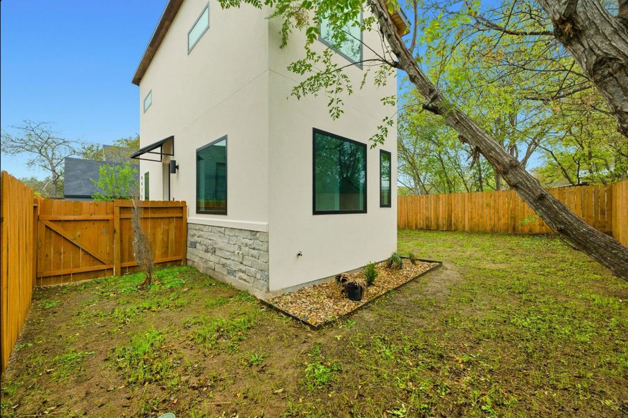 View of side of home featuring stone siding, a fenced backyard, stucco siding, and a gate View of side of home featuring stone siding, a fenced backyard, stucco siding, and a gate