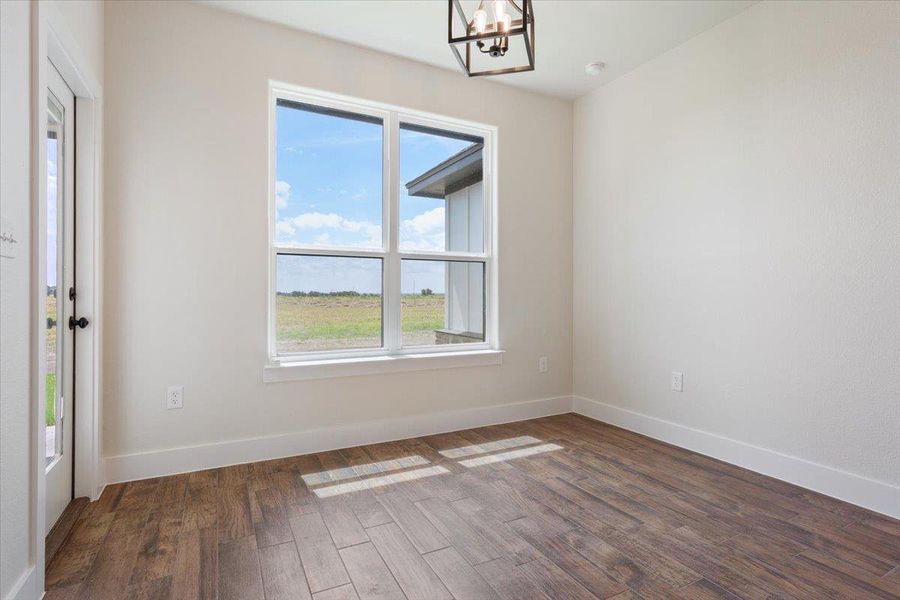A well-lit room showcases rich wood flooring and a panoramic window framing open fields.