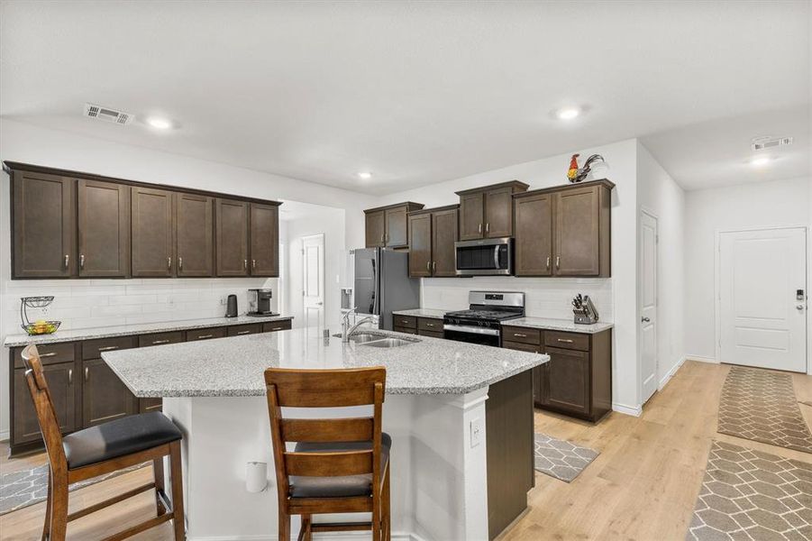 Kitchen featuring backsplash, dark brown cabinets, a breakfast bar, light wood-type flooring, and appliances with stainless steel finishes
