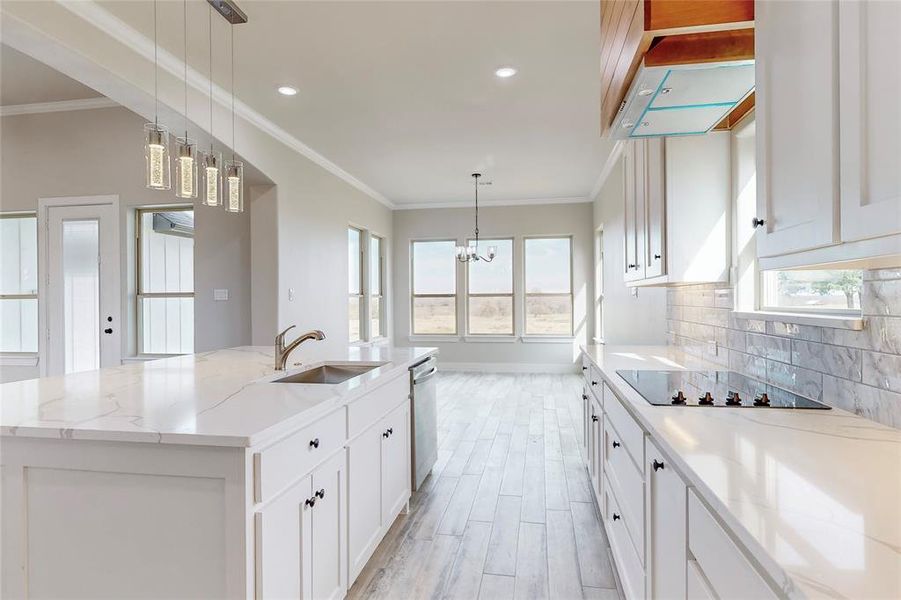 Kitchen featuring black electric stovetop, sink, pendant lighting, and an island with sink