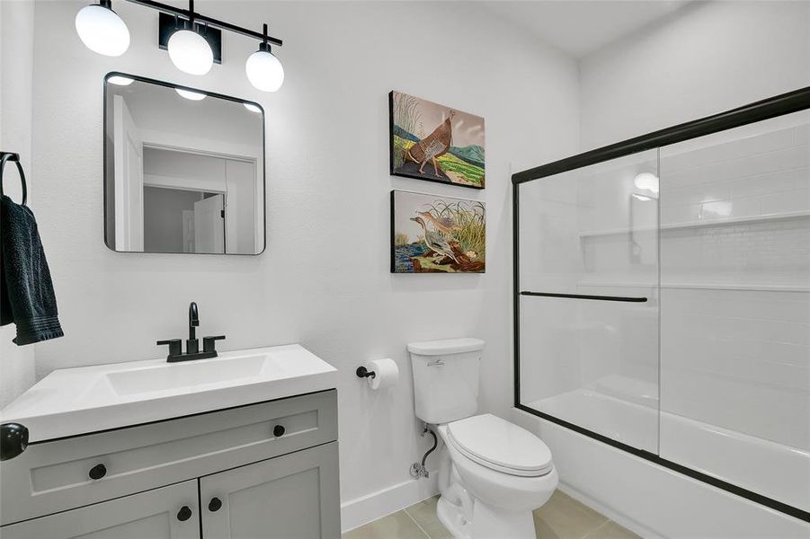 Full shared bathroom featuring tile and patterned flooring, enclosed tub / glass door shower combo, vanity, and toilet