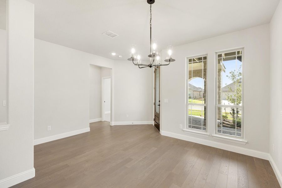 Empty dining room with hardwood floors, chandelier, and large windows overlooking a yard