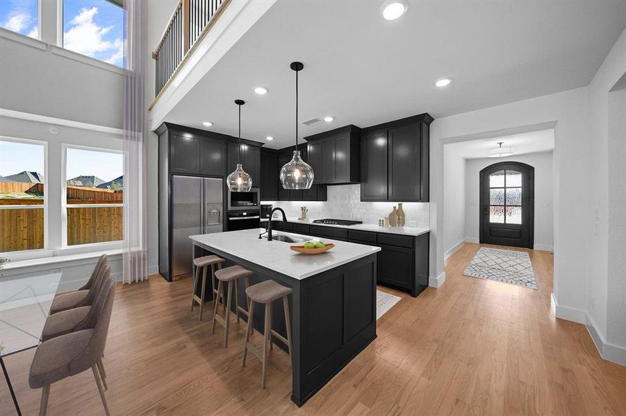 Kitchen with dark cabinetry, stainless steel appliances, a kitchen island with sink, hanging light fixtures, and recessed lighting Kitchen with dark cabinetry, stainless steel appliances, a kitchen island with sink, hanging light fixtures, and recessed lighting