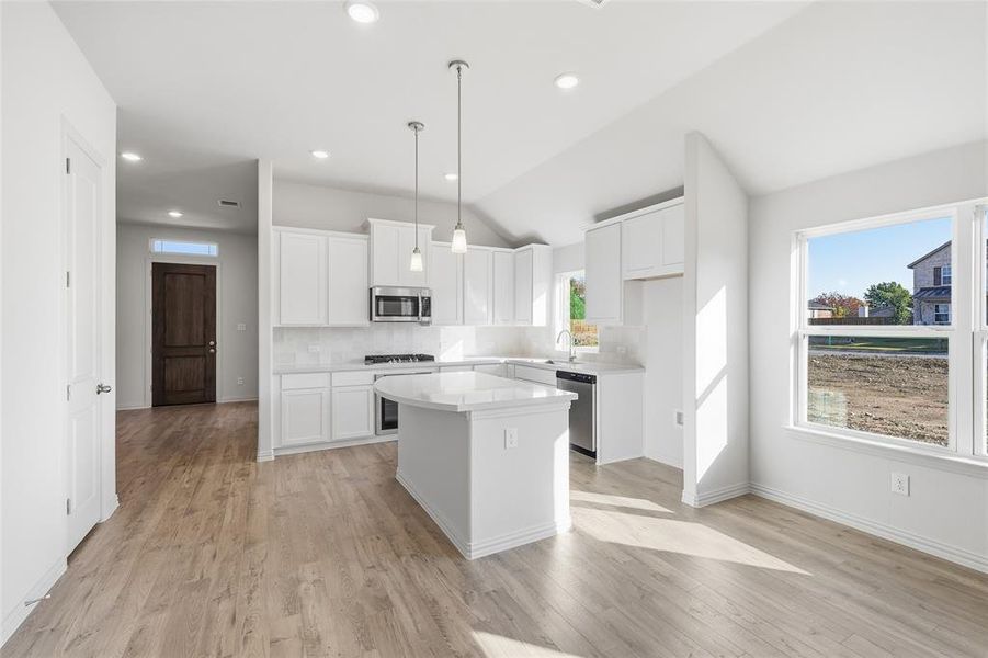 Kitchen featuring white cabinets, hanging light fixtures, a center island, vaulted ceiling, and light wood-style floors Kitchen featuring white cabinets, hanging light fixtures, a center island, vaulted ceiling, and light wood-style floors