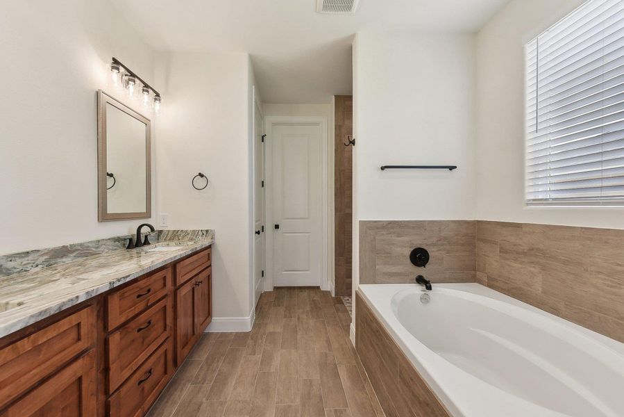 Full bath with vanity, wood finished floors, visible vents, baseboards, and a garden tub