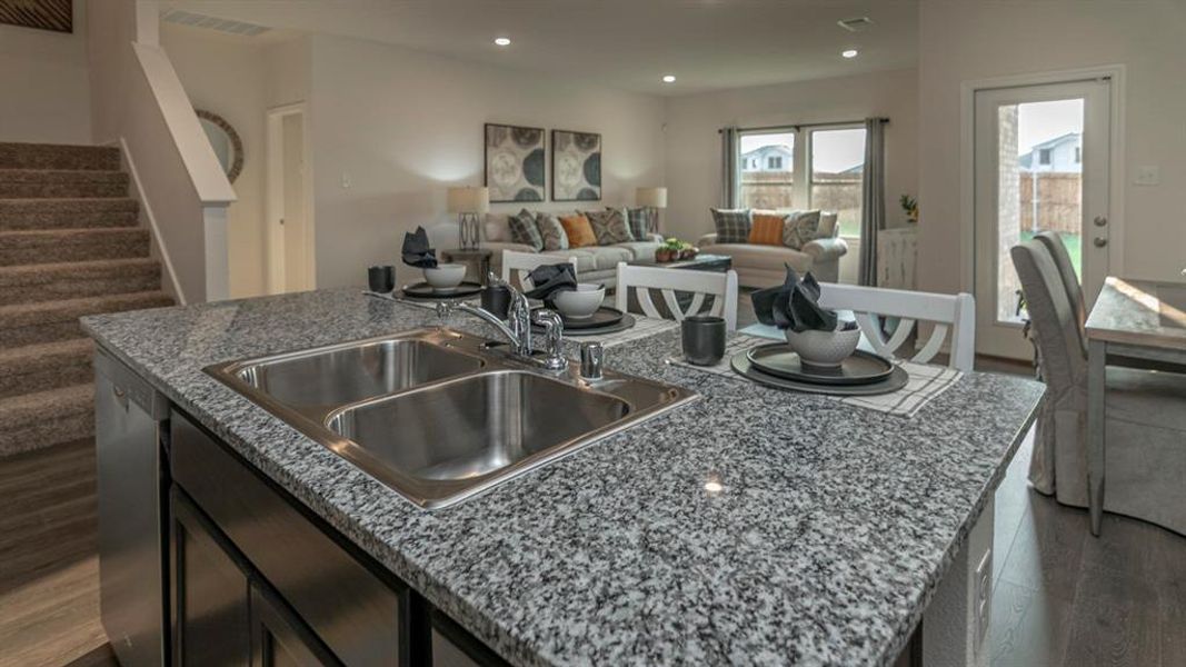 Kitchen island featuring a double-basin stainless steel sink, speckled granite countertop, and integrated dishwasher
