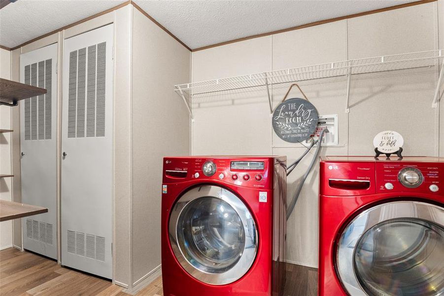 Laundry area with a textured ceiling, a heating unit, washing machine and dryer, wood finished floors, and crown molding