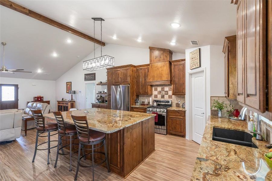 Open-concept kitchen featuring an oversized island with seating, rich wood cabinetry, stainless steel appliances, and granite countertops Open-concept kitchen featuring an oversized island with seating, rich wood cabinetry, stainless steel appliances, and granite countertops