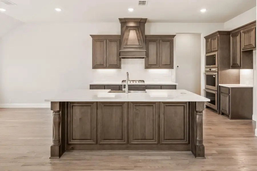 Kitchen with dark wood cabinets, large center island with white countertop, and custom range hood