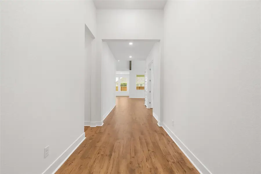 A long, clear hallway with rich wood flooring leads to naturally illuminated living spaces. A long, clear hallway with rich wood flooring leads to naturally illuminated living spaces.