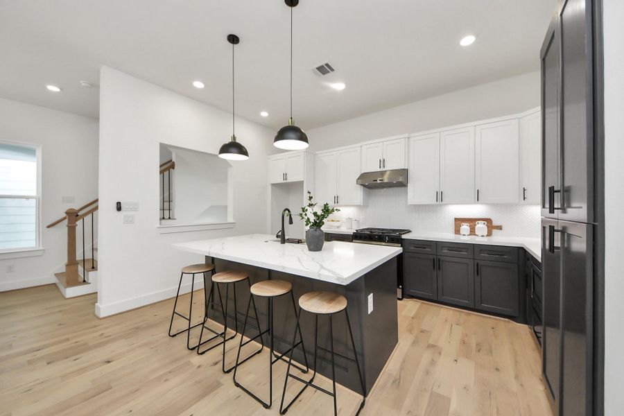 This photo showcases a modern kitchen with an open layout, featuring a large island with seating, sleek black and white cabinetry, and stainless steel appliances. The space is bright, with recessed lighting and pendant lights above the island, and adjacent to a staircase. This photo showcases a modern kitchen with an open layout, featuring a large island with seating, sleek black and white cabinetry, and stainless steel appliances. The space is bright, with recessed lighting and pendant lights above the island, and adjacent to a staircase.