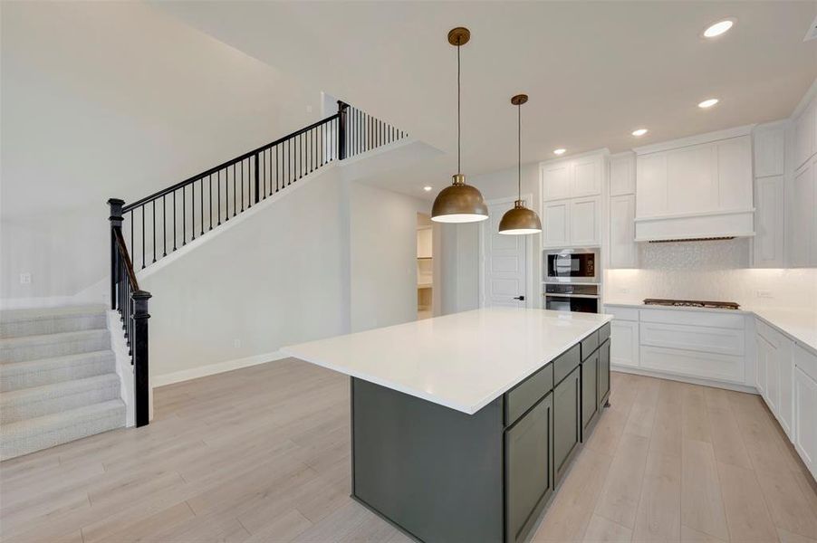 Two tone kitchen featuring two tone cabinets, backsplash, a kitchen island, light wood-style flooring, and hanging light fixtures