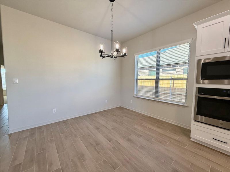 Kitchen featuring stainless steel appliances, wood finish floors, a chandelier, decorative light fixtures, and white cabinetry