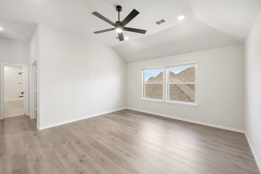 Empty bedroom with vaulted ceiling, black ceiling fan, light wood floors, and ensuite bathroom doorway Empty bedroom with vaulted ceiling, black ceiling fan, light wood floors, and ensuite bathroom doorway