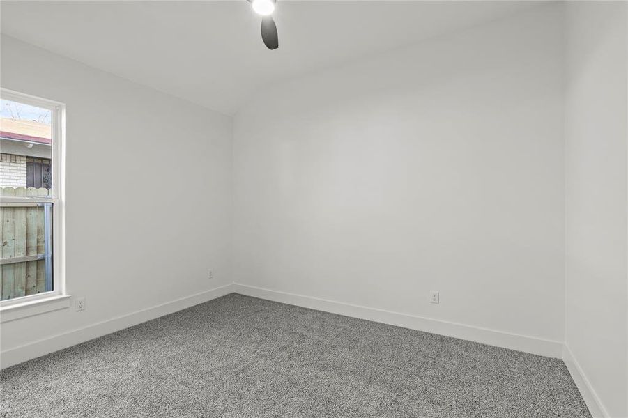 Carpeted empty room featuring ceiling fan and lofted ceiling