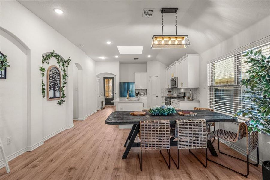 Dining room featuring lofted ceiling with skylight and light hardwood / wood-style flooring