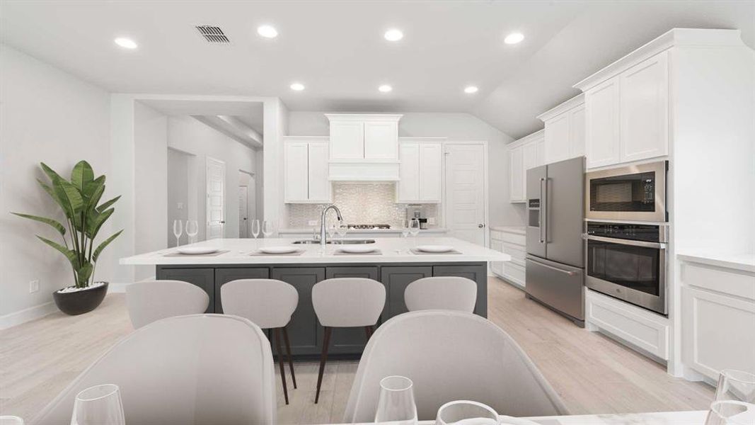 Kitchen with a center island with sink, light hardwood / wood-style flooring, stainless steel appliances, lofted ceiling, and white cabinets