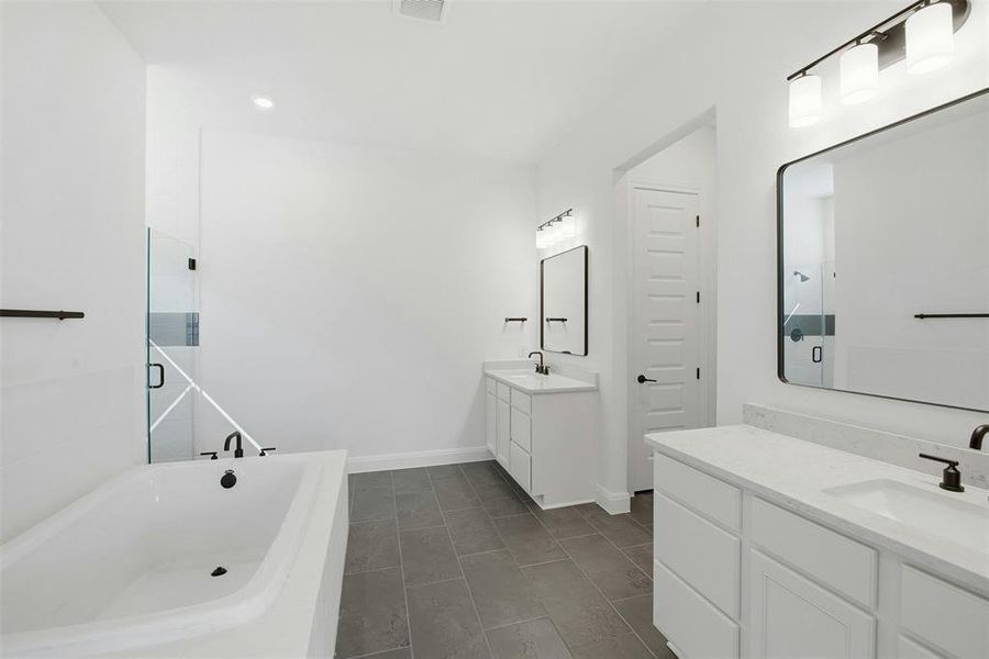 Spacious bathroom featuring dual vanities with white cabinetry and light-toned countertops, a built-in soaking tub with black fixtures, and a glass-enclosed shower