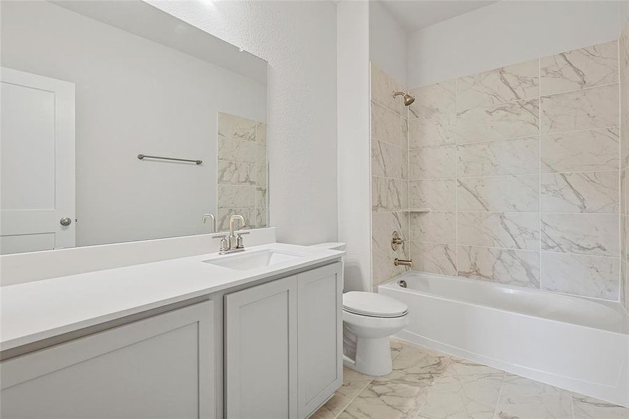 Bathroom featuring a vanity with a white countertop and a mirror, a toilet, a bathtub with a shower, and marble-patterned tile flooring and wall surround