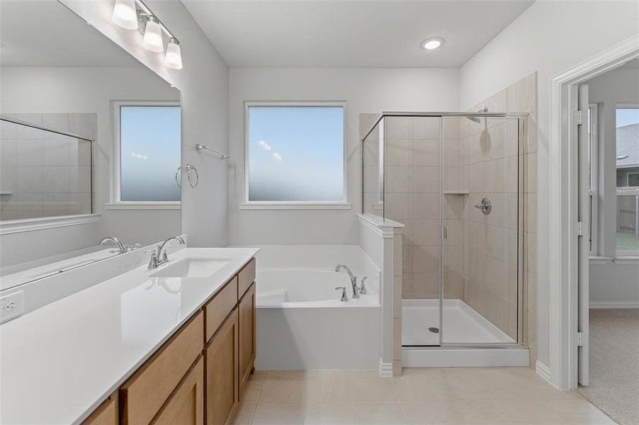 Bathroom featuring a double vanity with light wood-finish cabinetry, a large integrated mirror, an undermount soaking tub, a tiled walk-in shower with a glass enclosure, and two windows