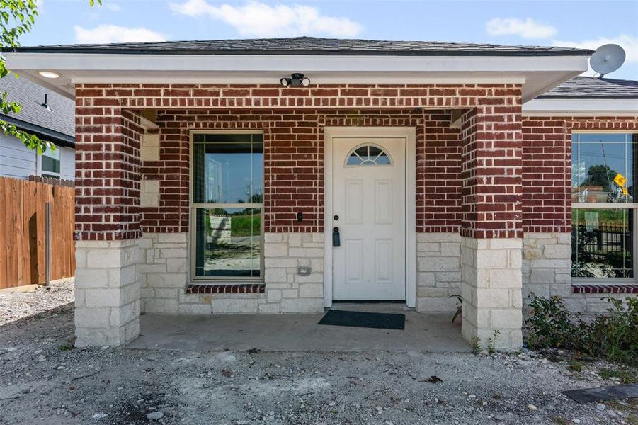 Property entrance with roof with shingles, a porch, and brick siding Property entrance with roof with shingles, a porch, and brick siding