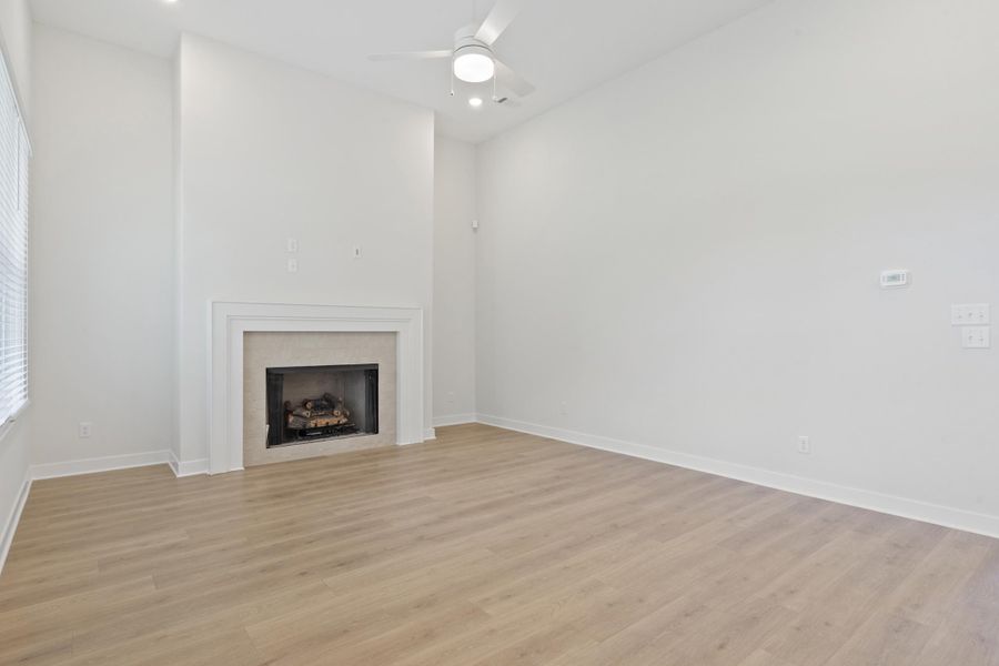 Spacious room featuring vaulted ceilings, wood-finish flooring, a fireplace with a stone surround, recessed lighting, and a ceiling fan