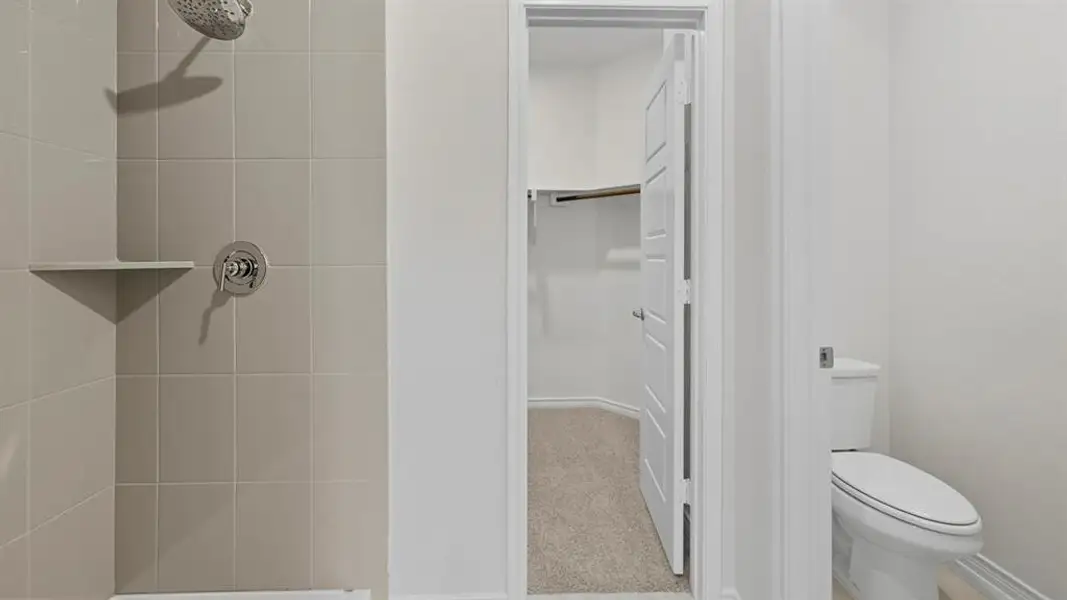 Full bathroom featuring tiled shower, light carpet, and a walk in closet Full bathroom featuring tiled shower, light carpet, and a walk in closet