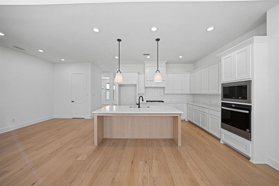 Kitchen with white cabinets, a kitchen island with sink, appliances with stainless steel finishes, light wood finished floors, and hanging light fixtures