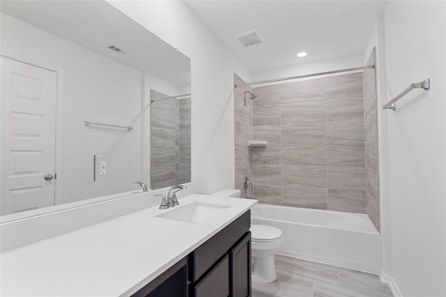 The secondary bathroom showcases tile flooring, a bath/shower combo with Daltile tile surround, a vanity with knee space and stunning light countertop, a stylish mirror, sleek fixtures, and contemporary finishes throughout. The secondary bathroom showcases tile flooring, a bath/shower combo with Daltile tile surround, a vanity with knee space and stunning light countertop, a stylish mirror, sleek fixtures, and contemporary finishes throughout.