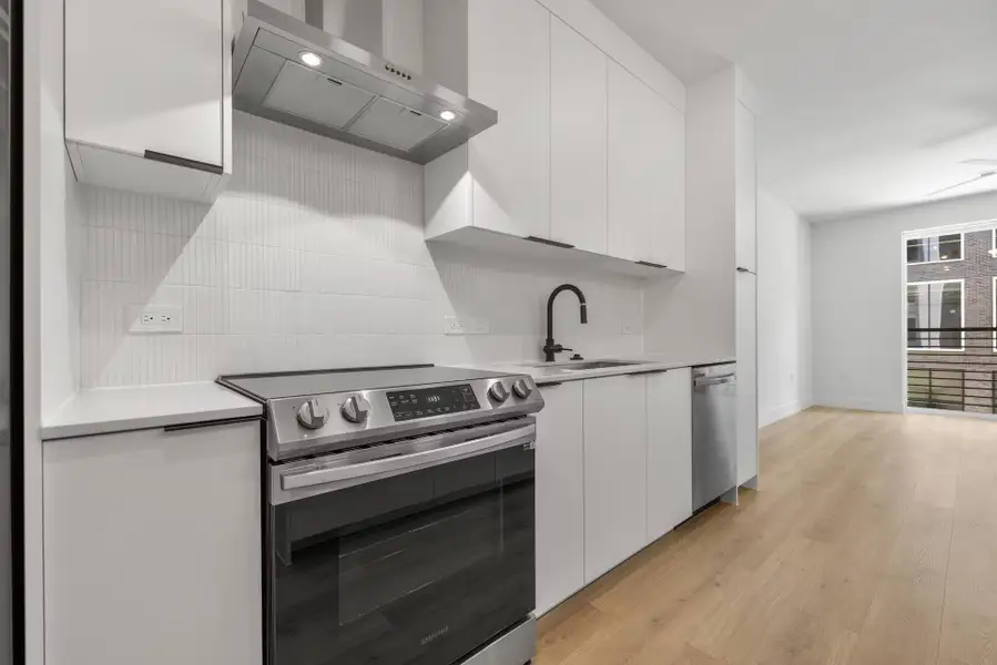 Kitchen with appliances with stainless steel finishes, under cabinet range hood, white cabinetry, and tasteful backsplash