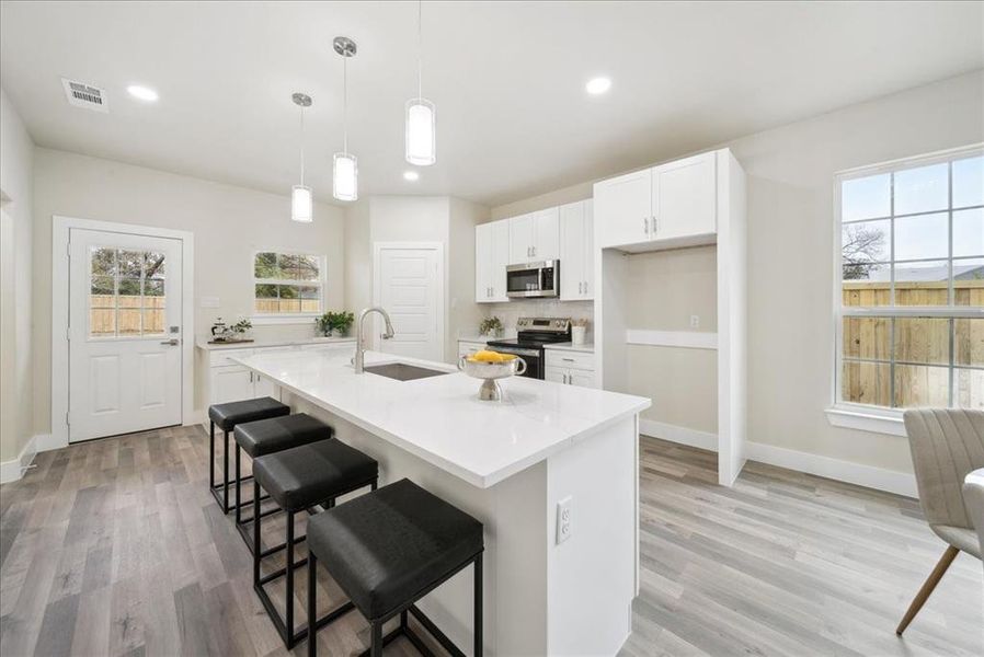 Kitchen featuring a kitchen island with sink, hanging light fixtures, sink, appliances with stainless steel finishes, and white cabinetry