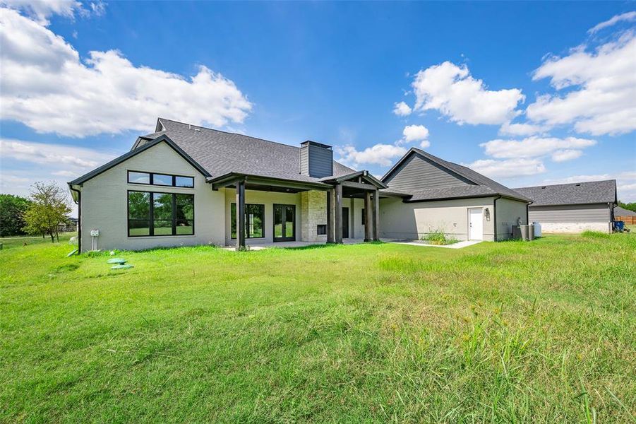 Rear view of house with a patio, a yard, a chimney, and a shingled roof