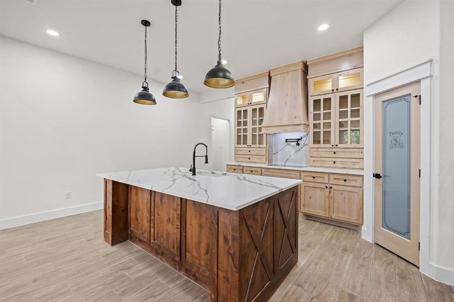 Kitchen featuring glass insert cabinets, light brown cabinets, decorative light fixtures, light wood-style flooring, and recessed lighting
