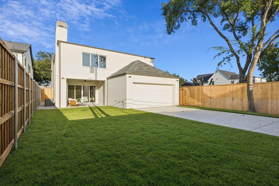 Back of house with stucco siding, concrete driveway, a fenced backyard, a garage, and a chimney