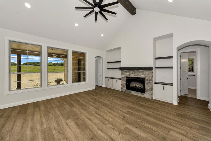 Unfurnished living room featuring healthy amount of natural light, a ceiling fan, arched walkways, beam ceiling, and wood finished floors