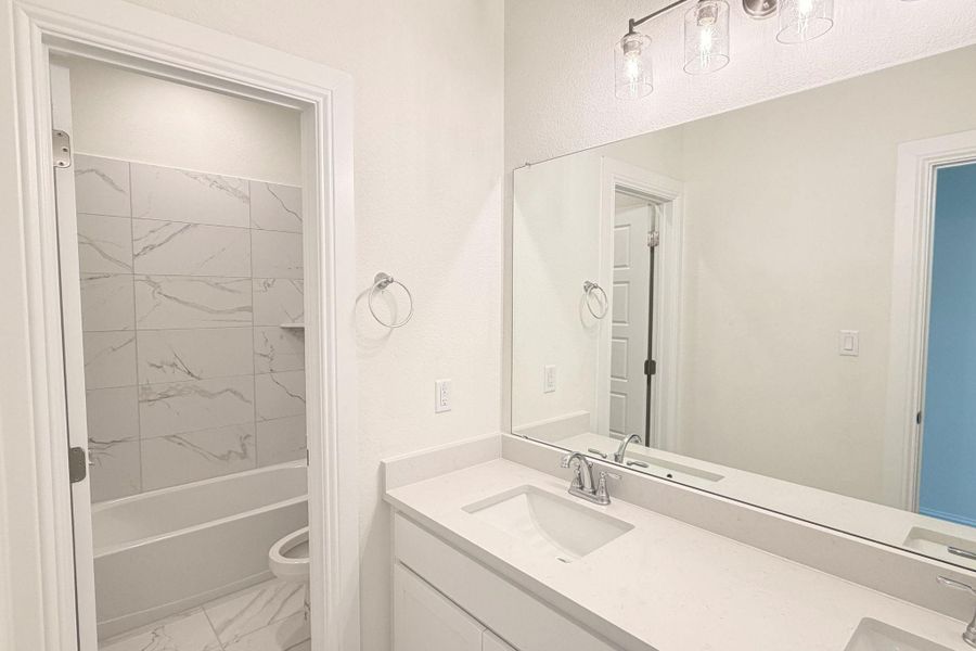 Full bathroom featuring double vanity, light marble finish floors, and shower / bath combination