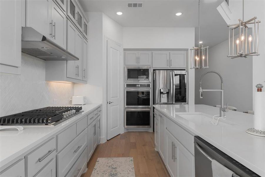 Kitchen featuring visible vents, stainless steel appliances, light wood-type flooring, under cabinet range hood, and a sink