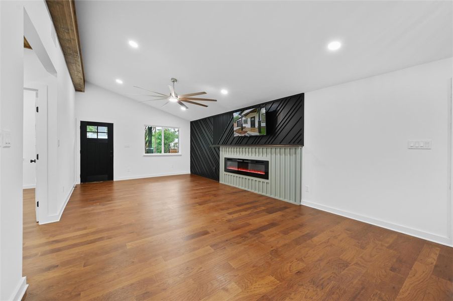 Unfurnished living room with wood finished floors, a glass covered fireplace, a ceiling fan, baseboards, and recessed lighting